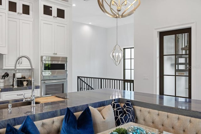 kitchen featuring multiple ovens, sink, pendant lighting, a chandelier, and white cabinetry