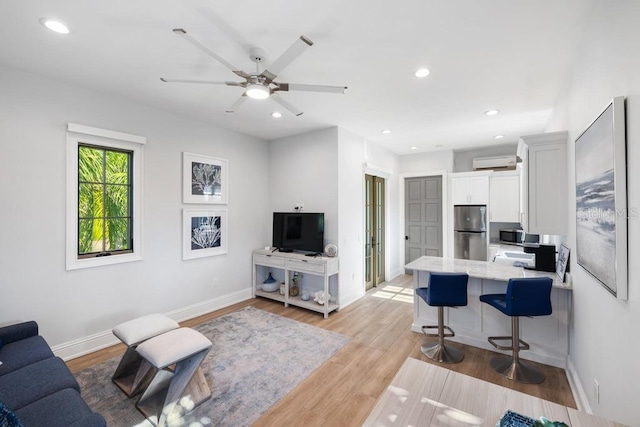 living room featuring a wall mounted AC, ceiling fan, and light hardwood / wood-style flooring