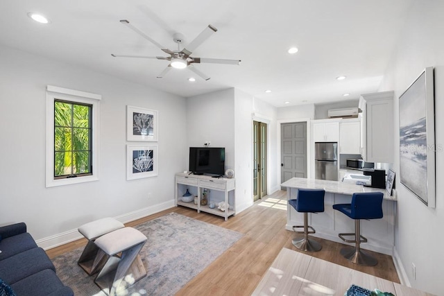 living room featuring ceiling fan, an AC wall unit, and light hardwood / wood-style floors