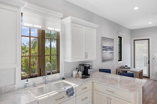 kitchen with light stone countertops, white cabinets, and sink