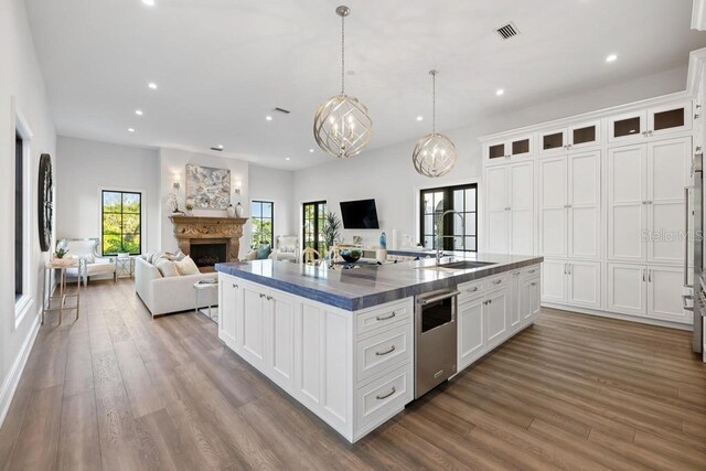 kitchen featuring hanging light fixtures, an island with sink, sink, and white cabinets