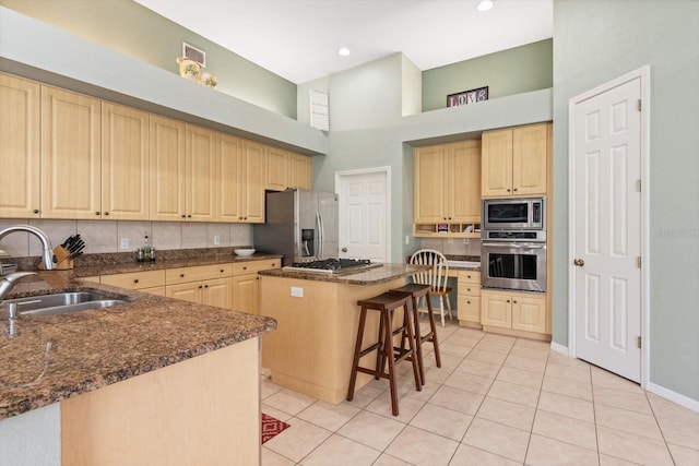 kitchen with a center island, sink, a towering ceiling, appliances with stainless steel finishes, and a breakfast bar area