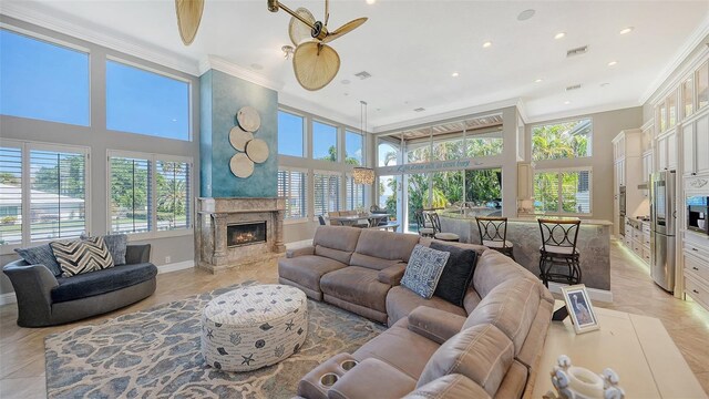 tiled living room featuring a towering ceiling, ceiling fan, a fireplace, and ornamental molding