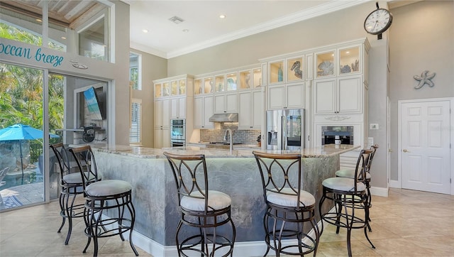 kitchen featuring white cabinetry, a kitchen bar, backsplash, light stone countertops, and appliances with stainless steel finishes