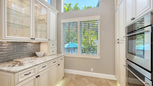 kitchen featuring light stone countertops, light tile patterned floors, backsplash, white cabinetry, and double oven