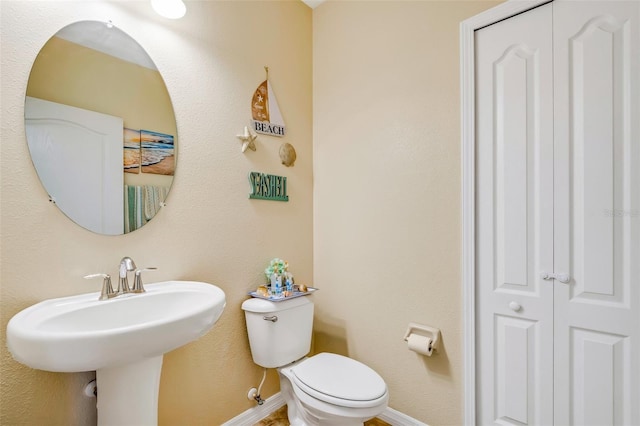 half bath with toilet, a sink, baseboards, and a closet