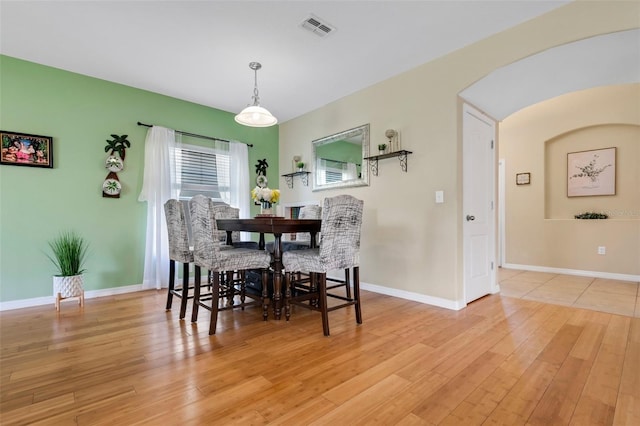 dining room with light wood-style floors, baseboards, visible vents, and arched walkways