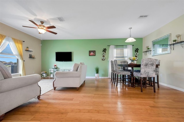 living room with light wood-type flooring, visible vents, ceiling fan, and baseboards