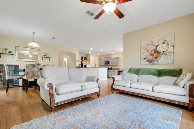 living area with light wood-style floors, ceiling fan, visible vents, and arched walkways