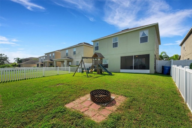 back of house featuring an outdoor fire pit, a lawn, a playground, and a fenced backyard