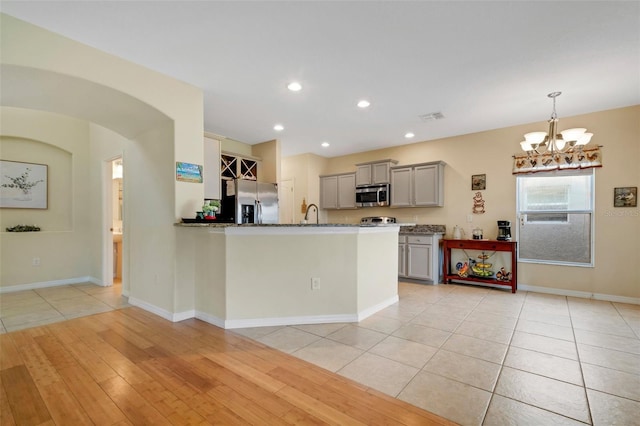 kitchen featuring arched walkways, gray cabinetry, stainless steel appliances, visible vents, and decorative light fixtures