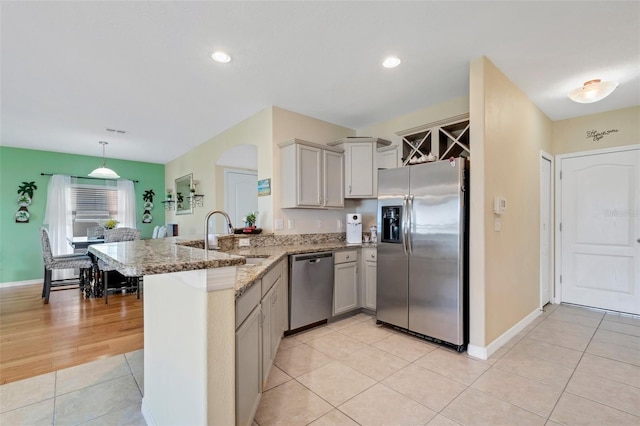 kitchen featuring stone countertops, a peninsula, hanging light fixtures, stainless steel appliances, and a sink