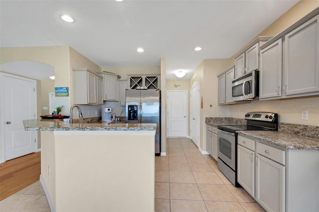 kitchen with appliances with stainless steel finishes, stone countertops, light tile patterned flooring, and gray cabinetry