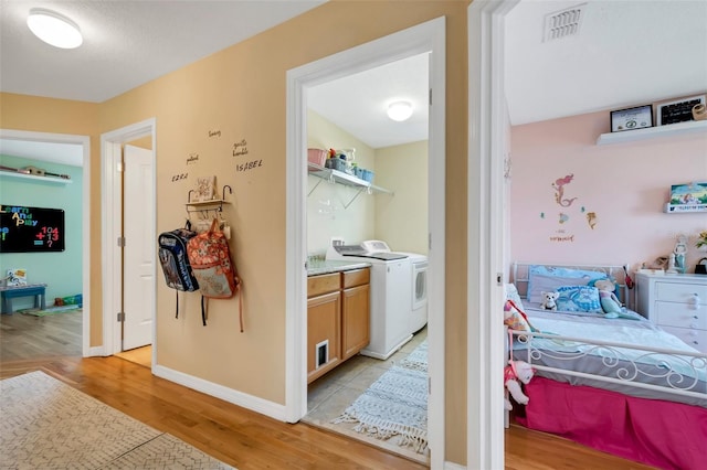 hallway featuring light wood-type flooring, visible vents, baseboards, and separate washer and dryer