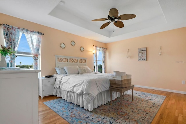 bedroom with a ceiling fan, a raised ceiling, baseboards, and light wood finished floors