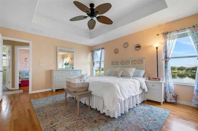 bedroom featuring a water view, light wood-style flooring, and a raised ceiling