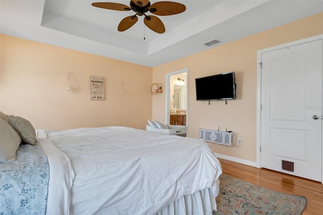 bedroom featuring wood finished floors, a ceiling fan, visible vents, baseboards, and a tray ceiling