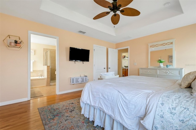 bedroom featuring visible vents, a raised ceiling, baseboards, light wood-style flooring, and ensuite bathroom