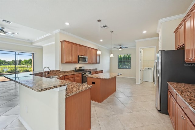 kitchen featuring stone counters, appliances with stainless steel finishes, washer / clothes dryer, hanging light fixtures, and a center island