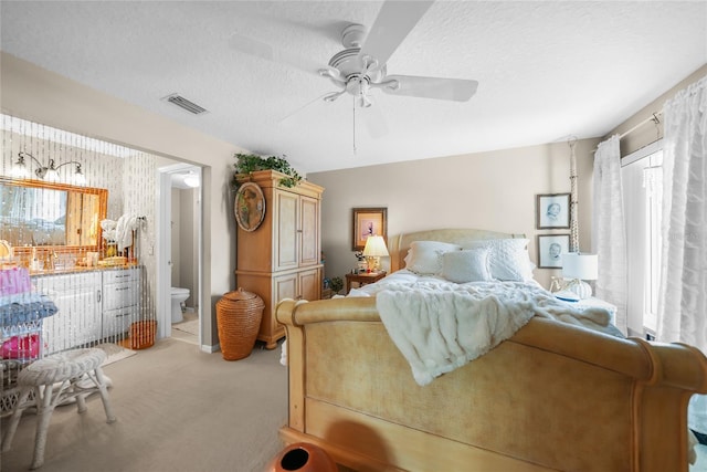 bedroom featuring a textured ceiling, light colored carpet, ensuite bathroom, and ceiling fan