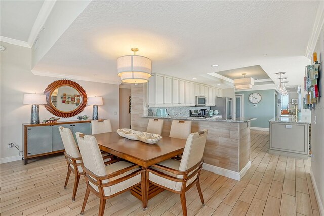 dining space featuring sink, ornamental molding, a raised ceiling, and a textured ceiling