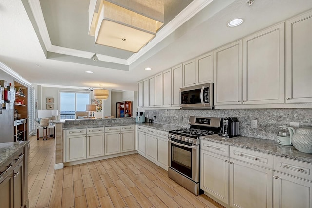 kitchen featuring light wood-type flooring, appliances with stainless steel finishes, a tray ceiling, kitchen peninsula, and decorative backsplash