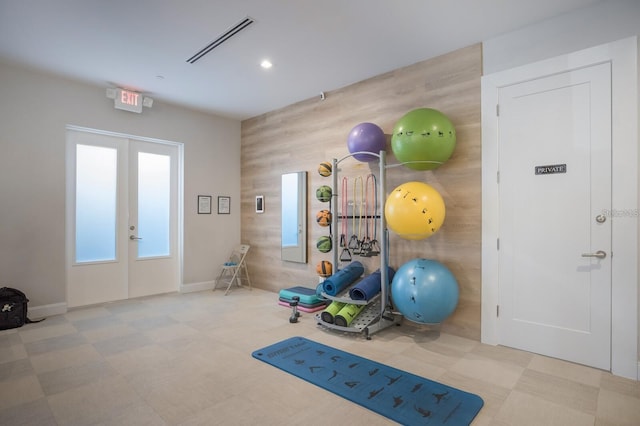 workout room with light tile patterned flooring, wood walls, and french doors