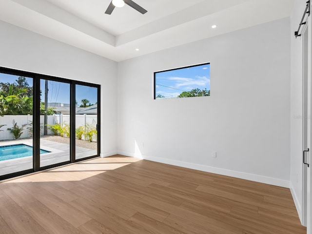 spare room featuring ceiling fan, a barn door, and light hardwood / wood-style floors