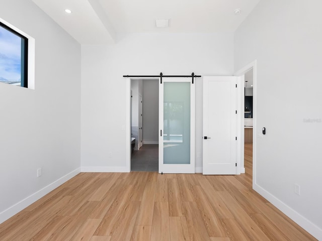 unfurnished bedroom with light wood-type flooring, ensuite bath, and a barn door