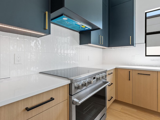 kitchen with stainless steel stove, wall chimney exhaust hood, light wood-type flooring, and tasteful backsplash