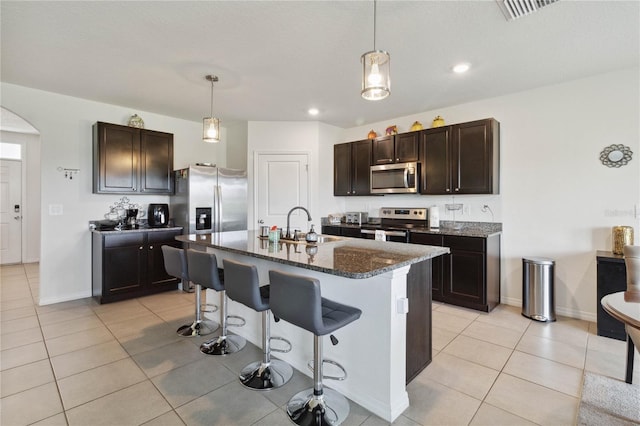 kitchen with light tile patterned flooring, sink, dark brown cabinets, a center island with sink, and appliances with stainless steel finishes