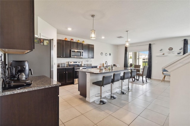 kitchen featuring a kitchen bar, decorative light fixtures, dark brown cabinets, a center island with sink, and stainless steel appliances