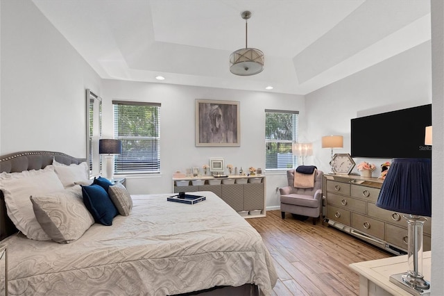 bedroom featuring light hardwood / wood-style flooring, a raised ceiling, and multiple windows