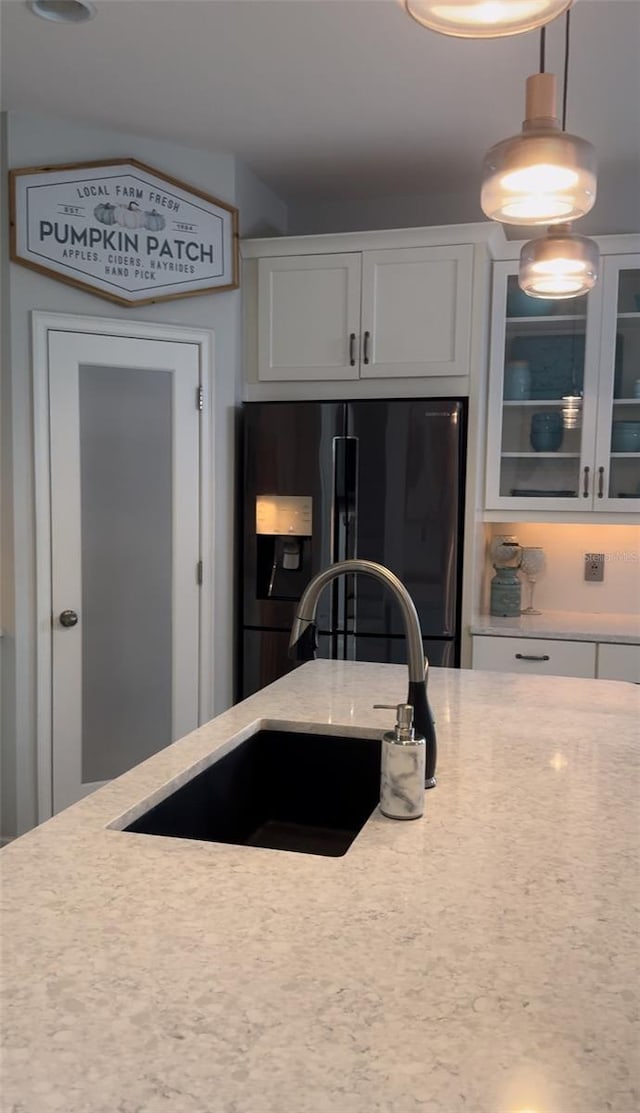 5228 Bentgrass Way, Bradenton, FL 34211 - kitchen featuring black fridge with ice dispenser, glass insert cabinets, white cabinetry, light stone countertops, and pendant lighting