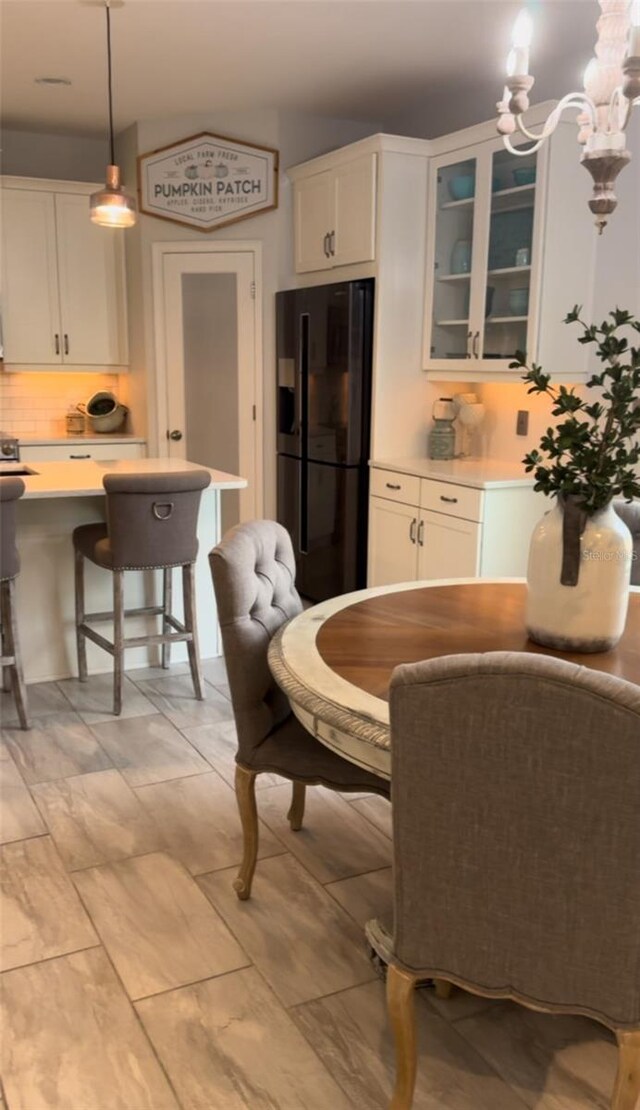 kitchen featuring white cabinetry, hanging light fixtures, a breakfast bar, tasteful backsplash, and black fridge