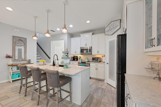 kitchen with white cabinets, hanging light fixtures, appliances with stainless steel finishes, and a kitchen island with sink