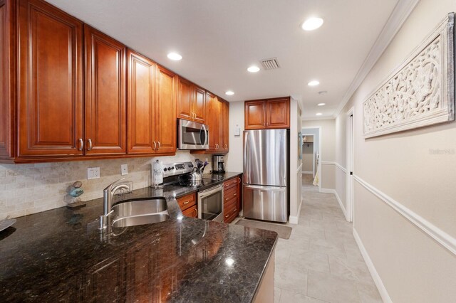 kitchen with tasteful backsplash, dark stone counters, ornamental molding, stainless steel appliances, and sink