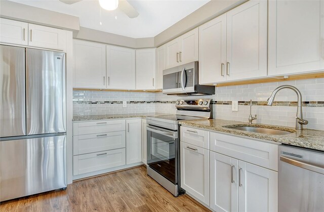 kitchen with appliances with stainless steel finishes, white cabinetry, sink, decorative backsplash, and light hardwood / wood-style flooring