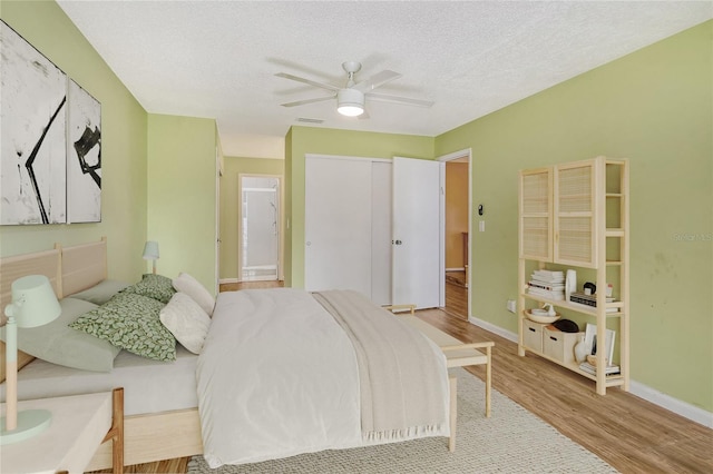 bedroom with ceiling fan, a closet, light hardwood / wood-style floors, and a textured ceiling