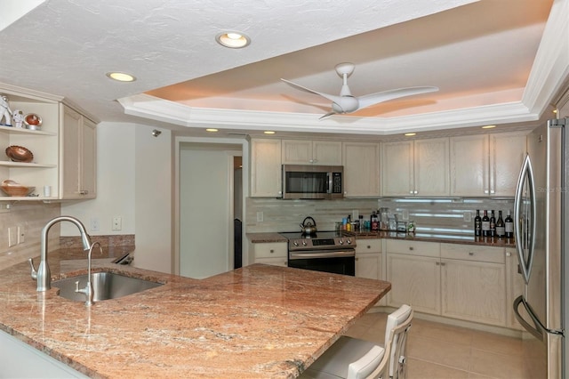 kitchen featuring sink, appliances with stainless steel finishes, a tray ceiling, light stone countertops, and kitchen peninsula