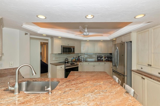 kitchen featuring a raised ceiling, appliances with stainless steel finishes, sink, and cream cabinetry