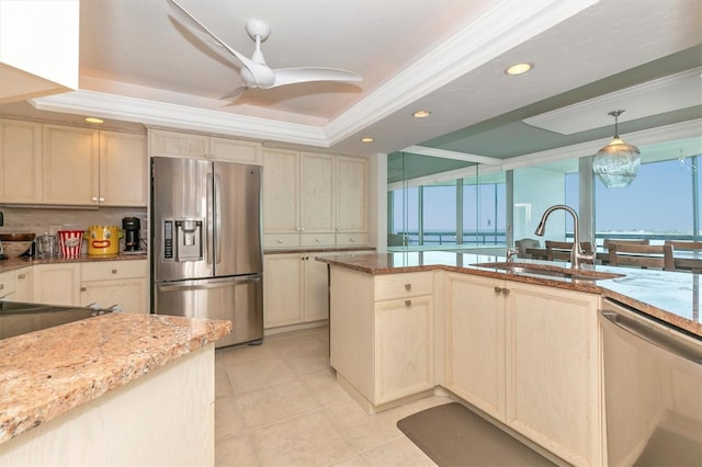 kitchen with sink, appliances with stainless steel finishes, a raised ceiling, pendant lighting, and light stone countertops