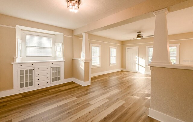 unfurnished living room featuring ornate columns, ceiling fan, and light wood-type flooring