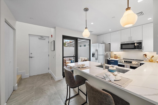 kitchen featuring appliances with stainless steel finishes, sink, white cabinetry, and decorative light fixtures