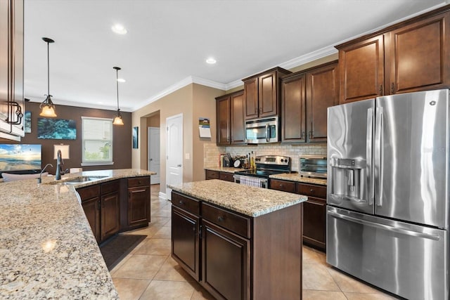 kitchen with sink, stainless steel appliances, decorative light fixtures, ornamental molding, and a kitchen island with sink