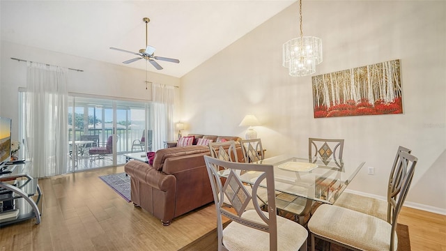 dining space with high vaulted ceiling, ceiling fan with notable chandelier, and light hardwood / wood-style floors