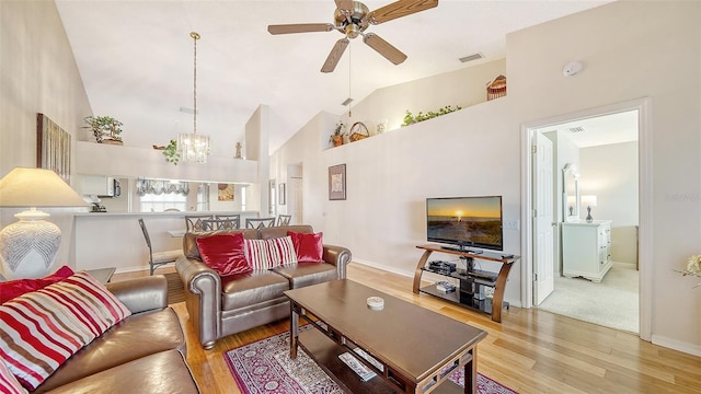 carpeted living room featuring ceiling fan with notable chandelier and high vaulted ceiling