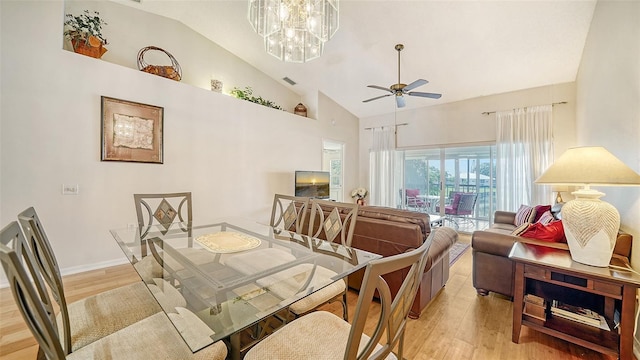 dining space featuring ceiling fan with notable chandelier, high vaulted ceiling, and light hardwood / wood-style floors