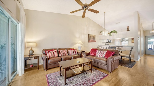 living room with light wood-type flooring, ceiling fan with notable chandelier, and high vaulted ceiling