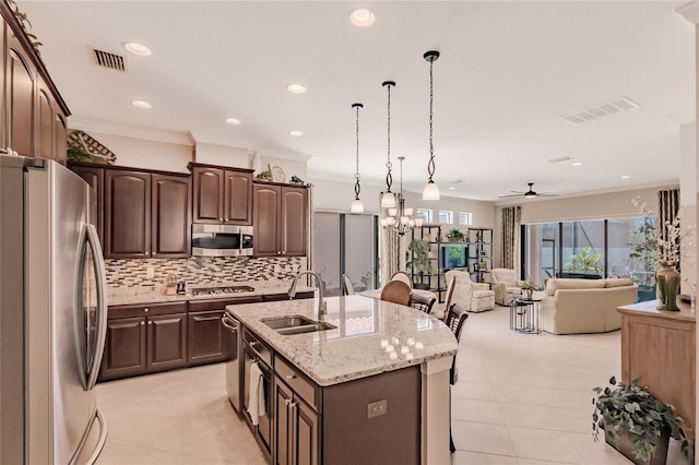 kitchen featuring stainless steel appliances, crown molding, sink, pendant lighting, and an island with sink